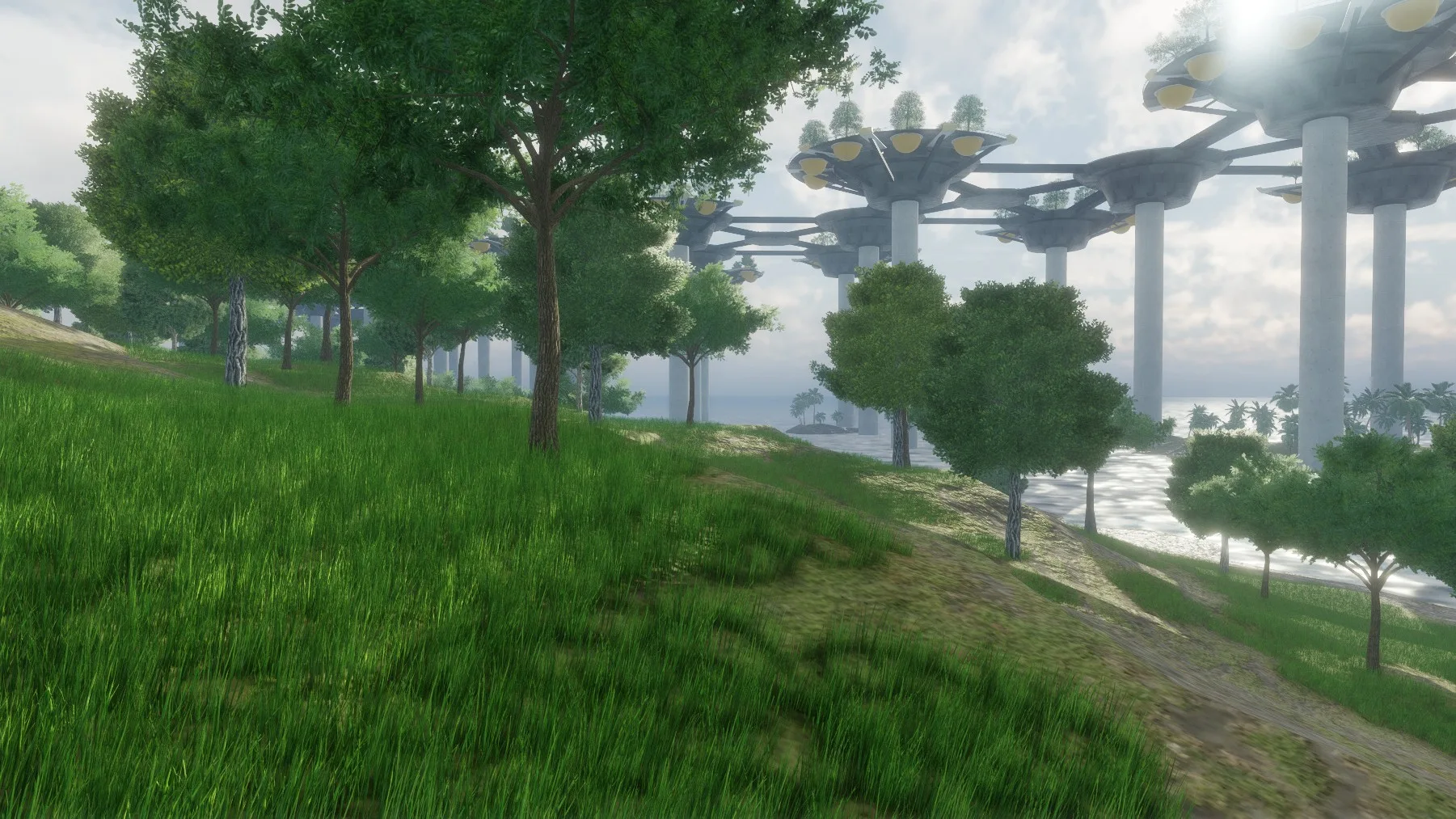A grassy path among trees, with raised round platforms on pillars in the distance by the water.